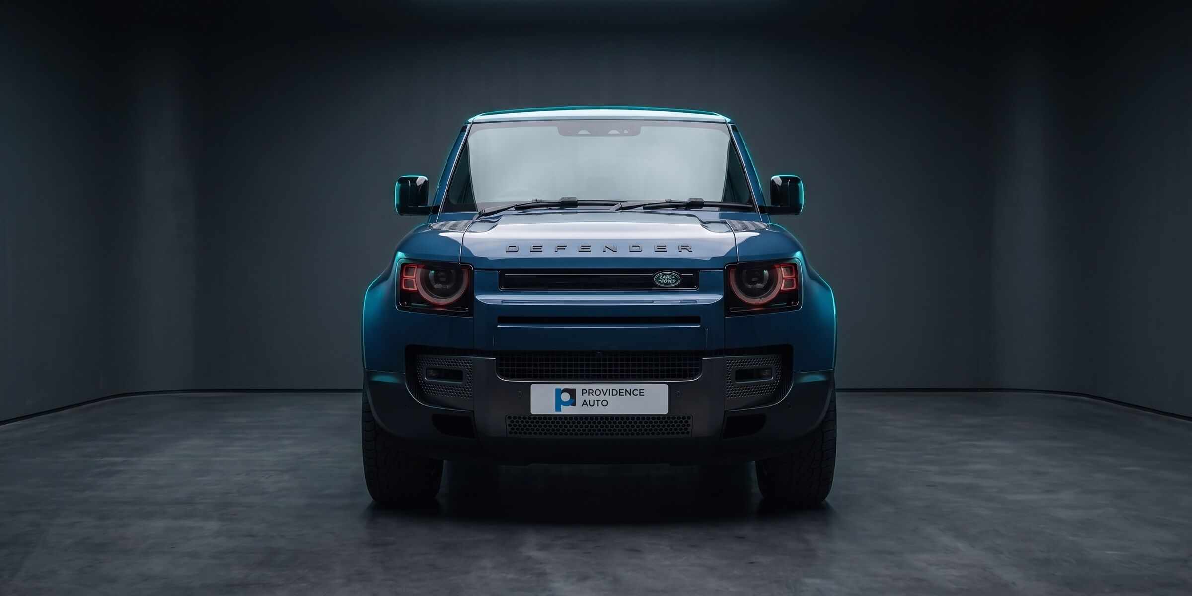 A blue Land Rover Defender in a dark studio, the Providence Auto plate on its front bumper